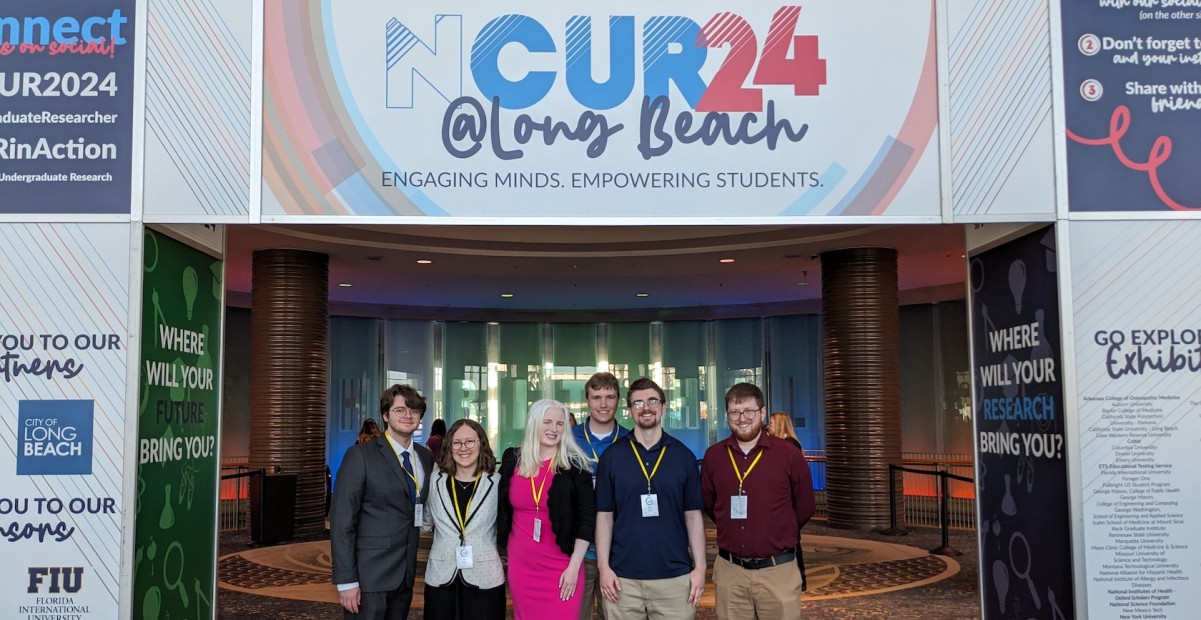 IC students who presented at NCUR standing underneath the NCUR 2024 banner