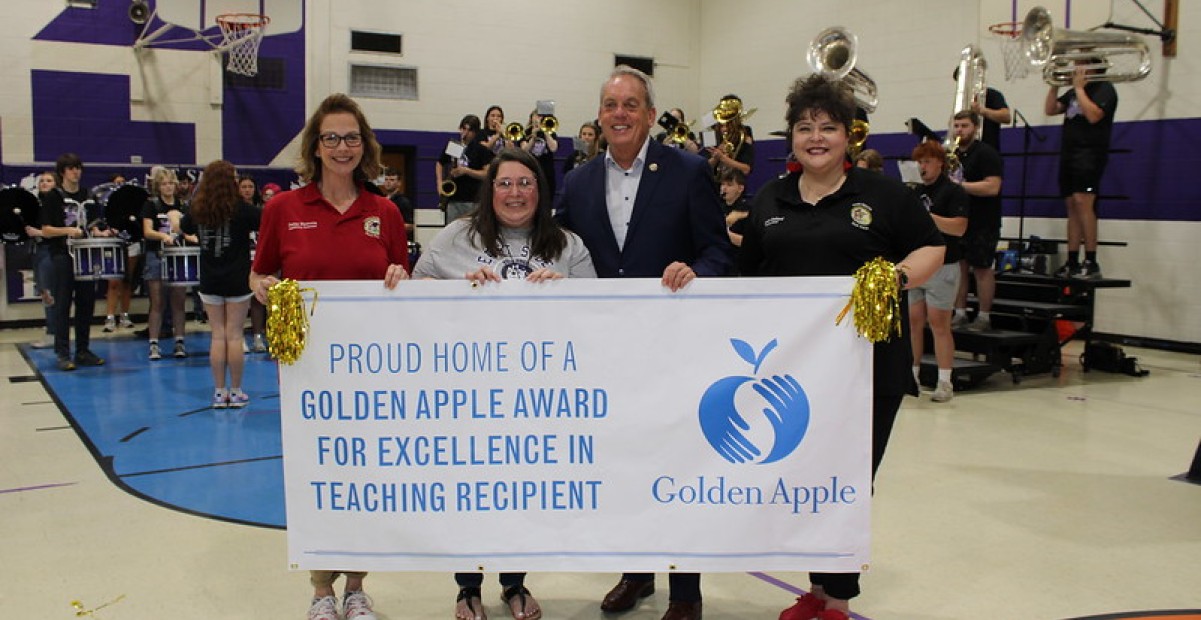 Illinois College alumna Christina Beck '04 posing at school with Golden Apple banner