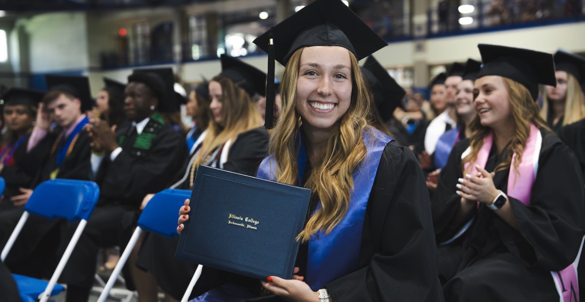 Student smiling and posing with diploma at graduation