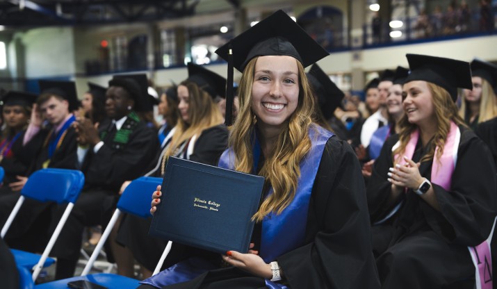 Student smiling and posing with diploma at graduation